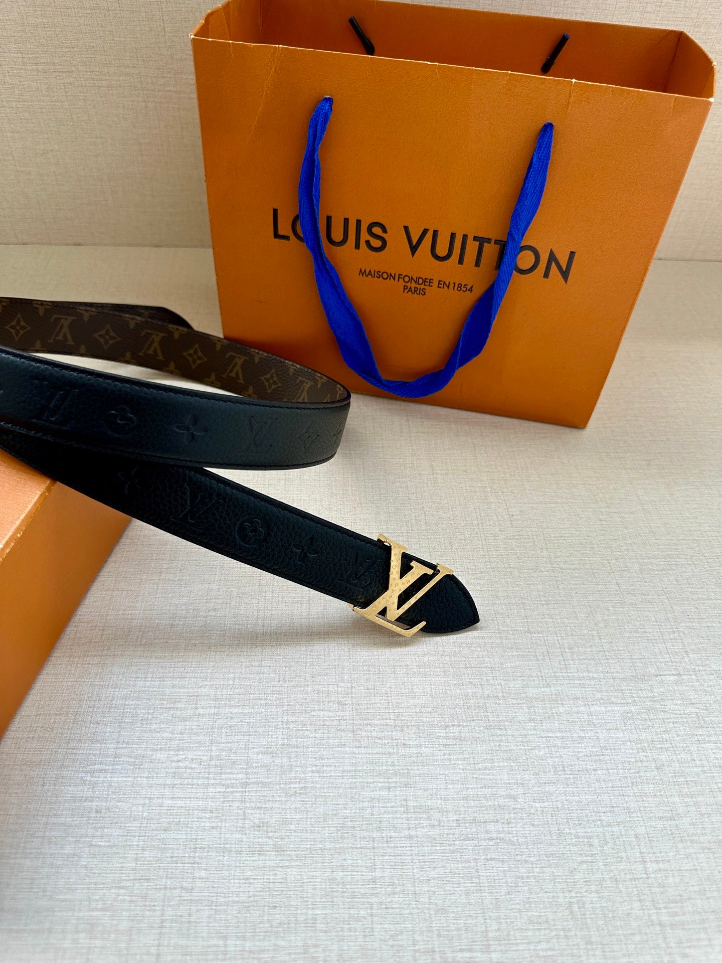 Monogram belt with dark strap and gold-tone LV buckle laid on a surface