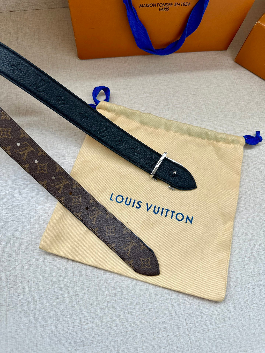 Monogram belt straps with LV buckle and metal pin on a beige pouch