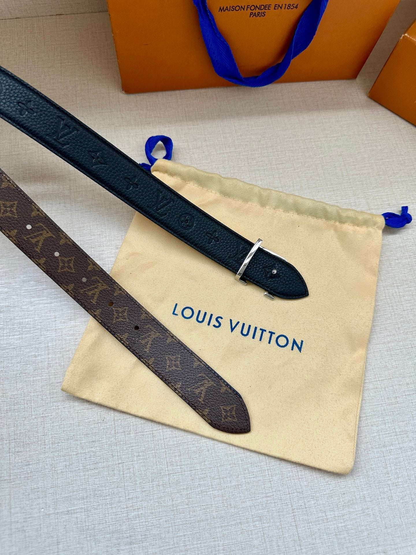 Monogram belt straps with LV buckle and metal pin on a beige pouch