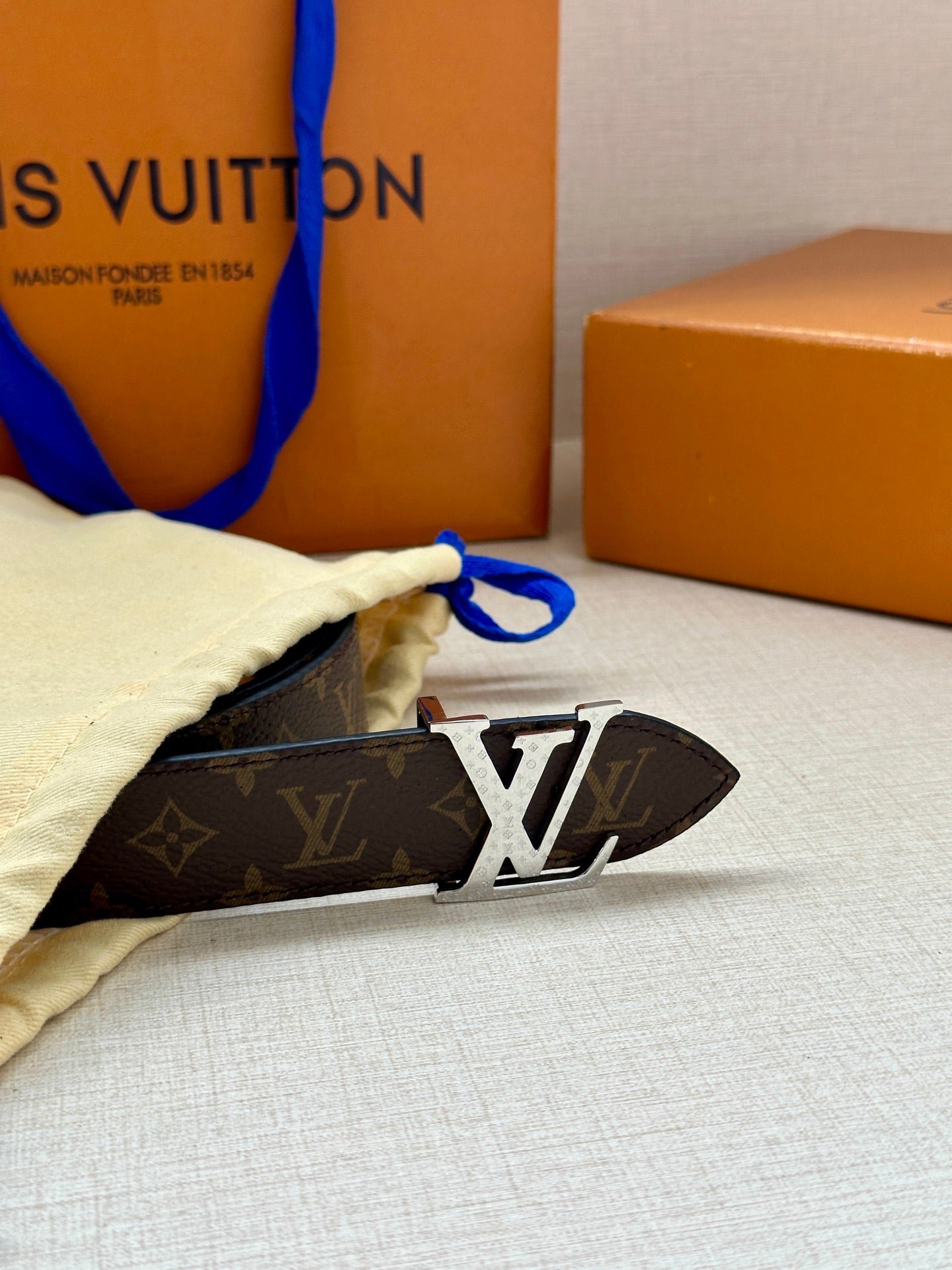 Monogram belt with dark strap and gold-tone LV buckle on beige cloth pouch