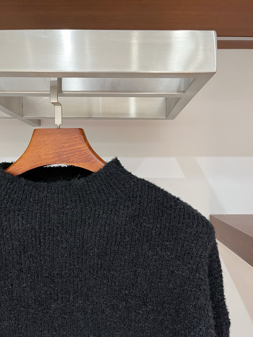 Dark textured long-sleeve sweater with crew neck, side view on hanger