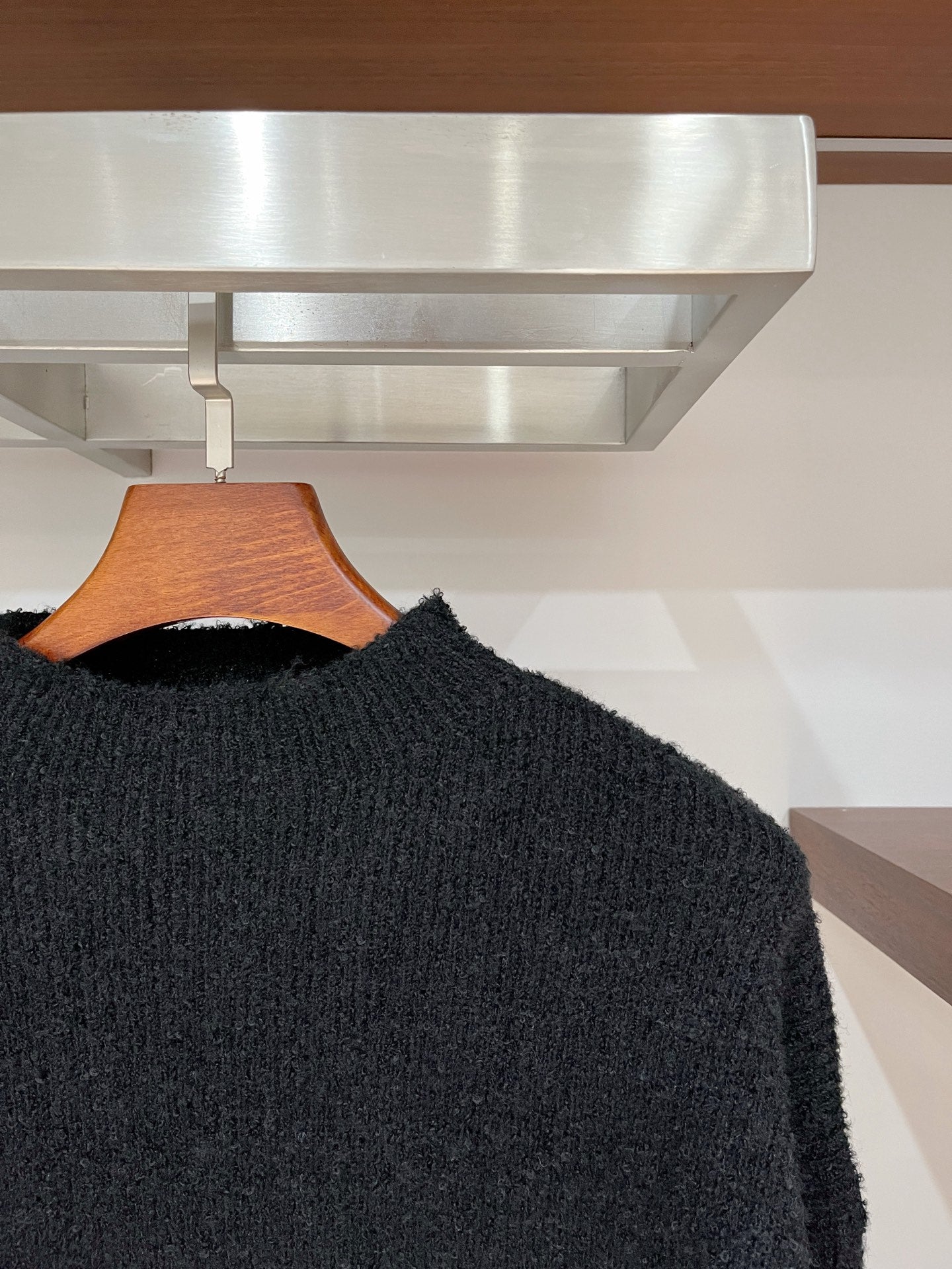 Dark textured long-sleeve sweater with crew neck, side view on hanger