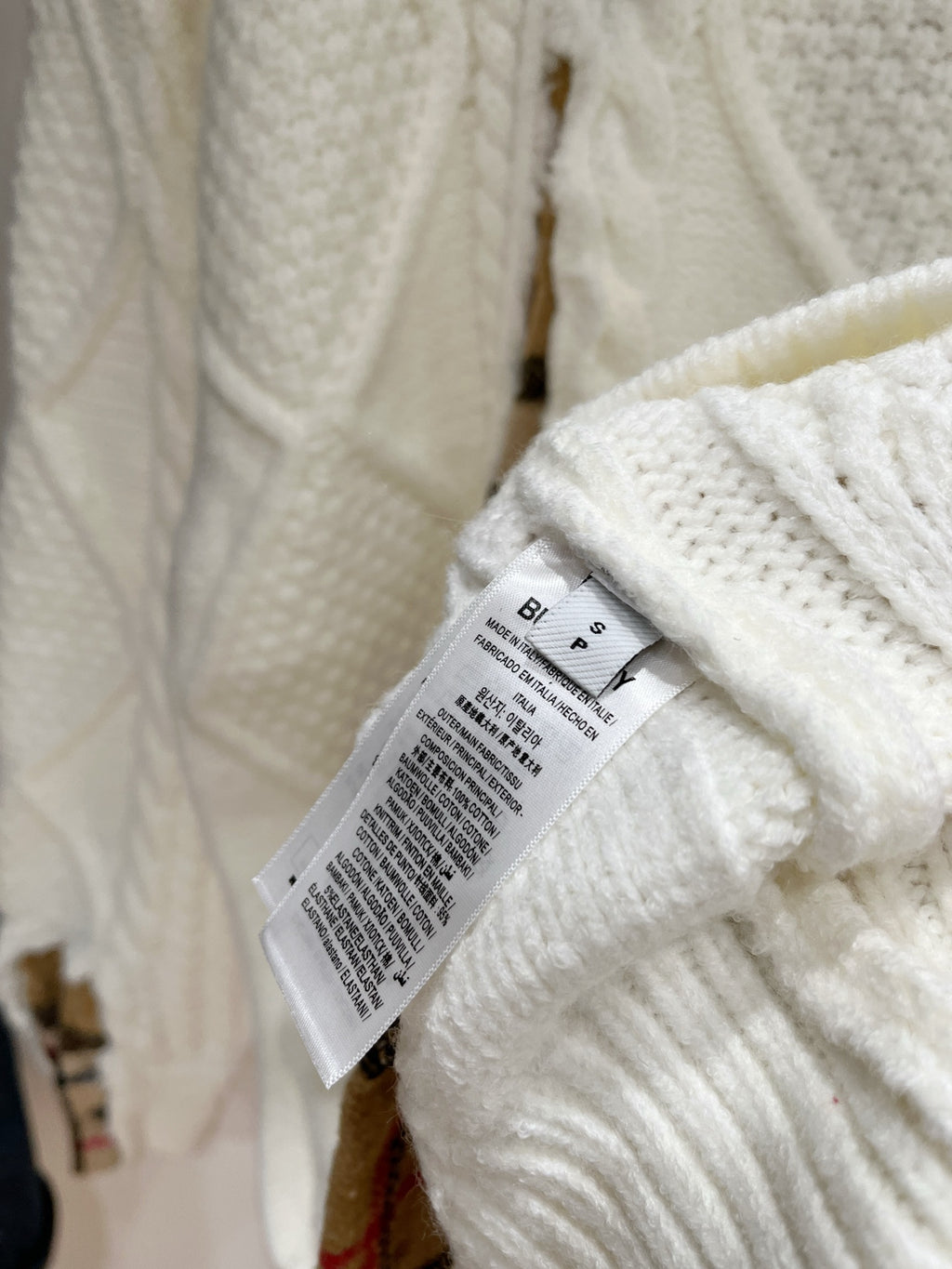 Cream knit sweater with white size/care label and knit texture near seam