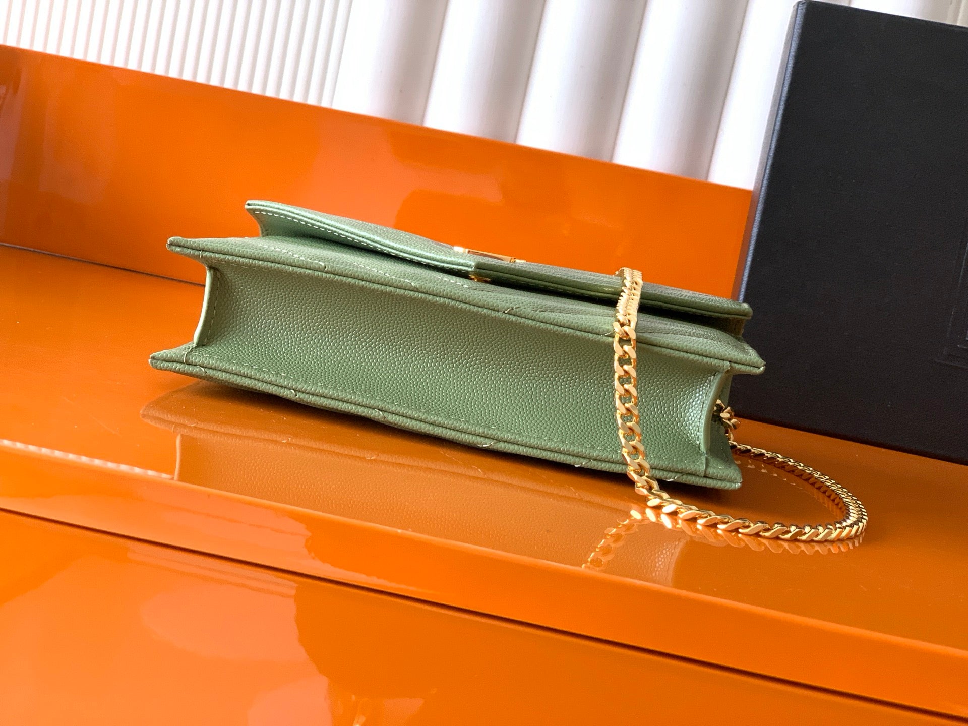Green leather YSL bag with flap and gold chain strap on open top edge
