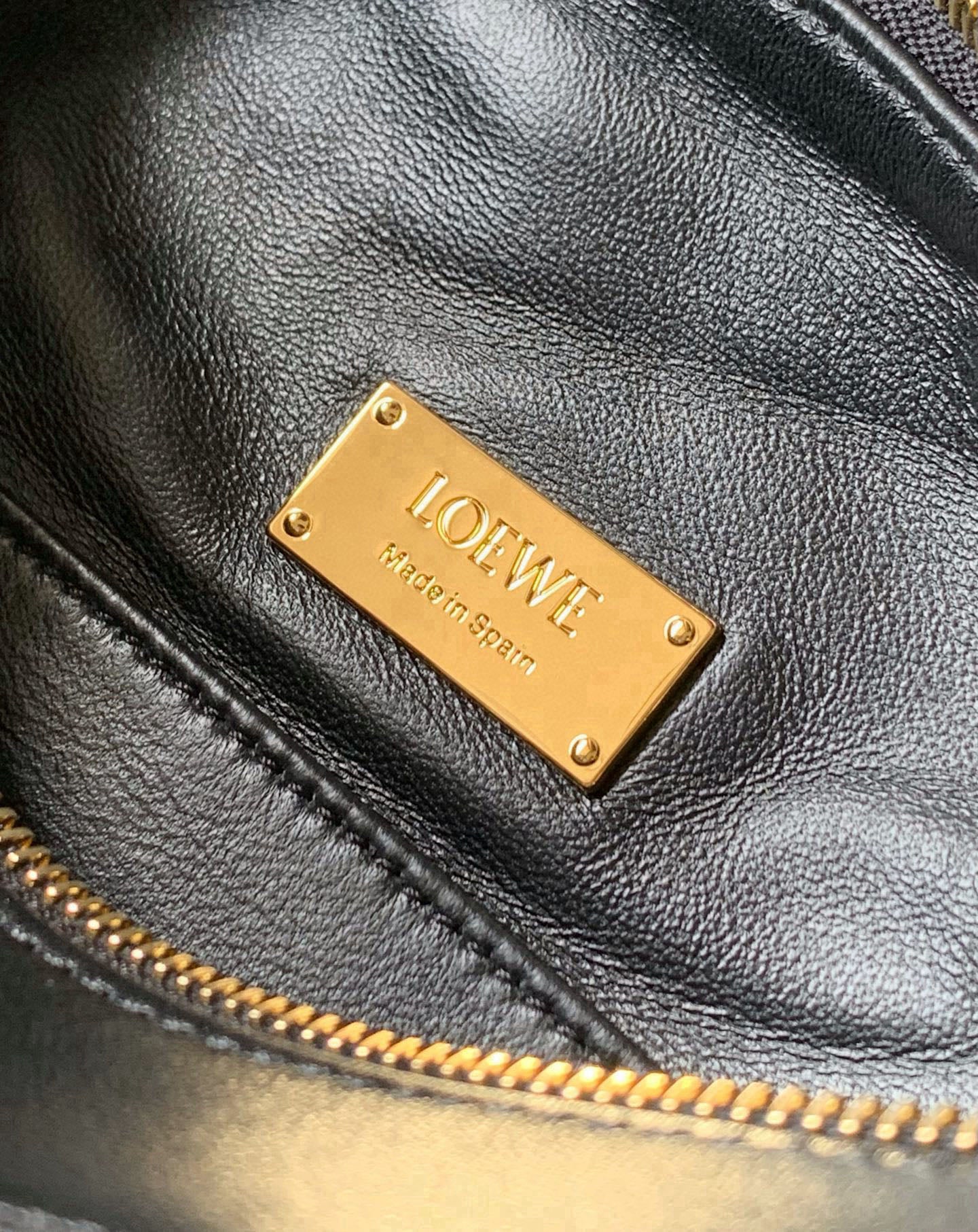 Black leather bag with gold nameplate, stitched edge, and zipper trim