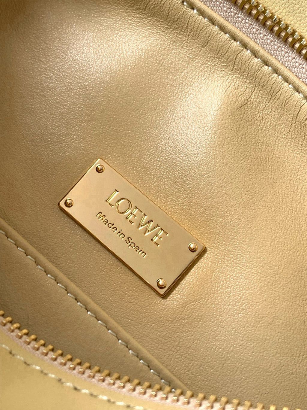 Loewe light yellow leather bag close-up with metal logo nameplate and zipper seam