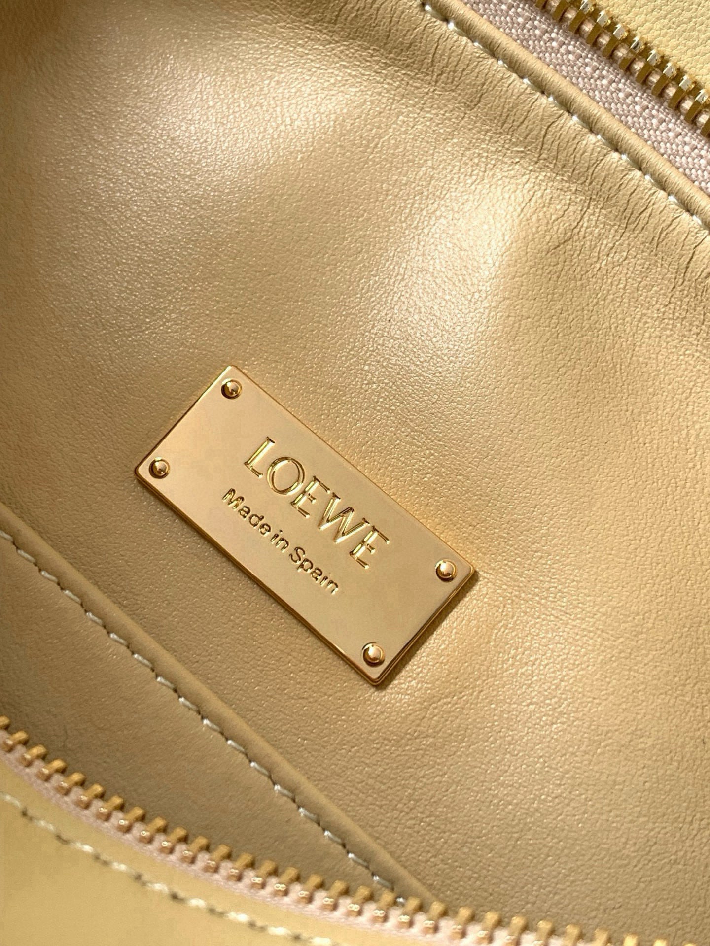 Loewe light yellow leather bag close-up with metal logo nameplate and zipper seam