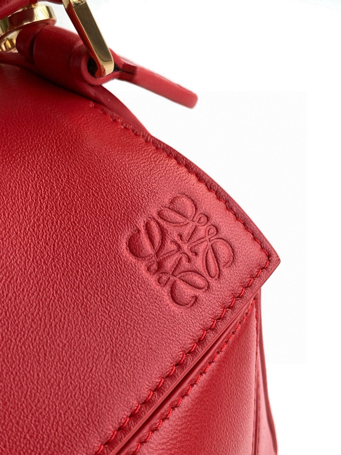 Red leather bag corner with embossed logo and stitched edge detail