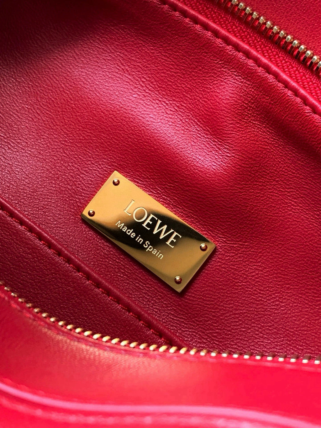 Loewe red leather bag close-up with gold logo plaque and zipper edge