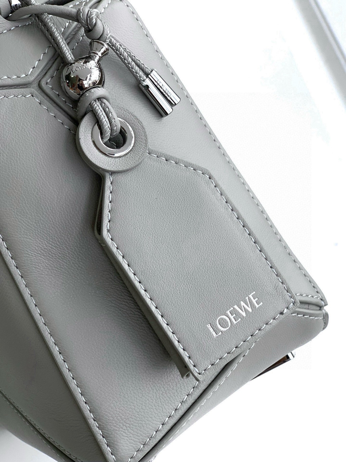 Light gray leather bag side detail with metal ring clasp and stitched panel