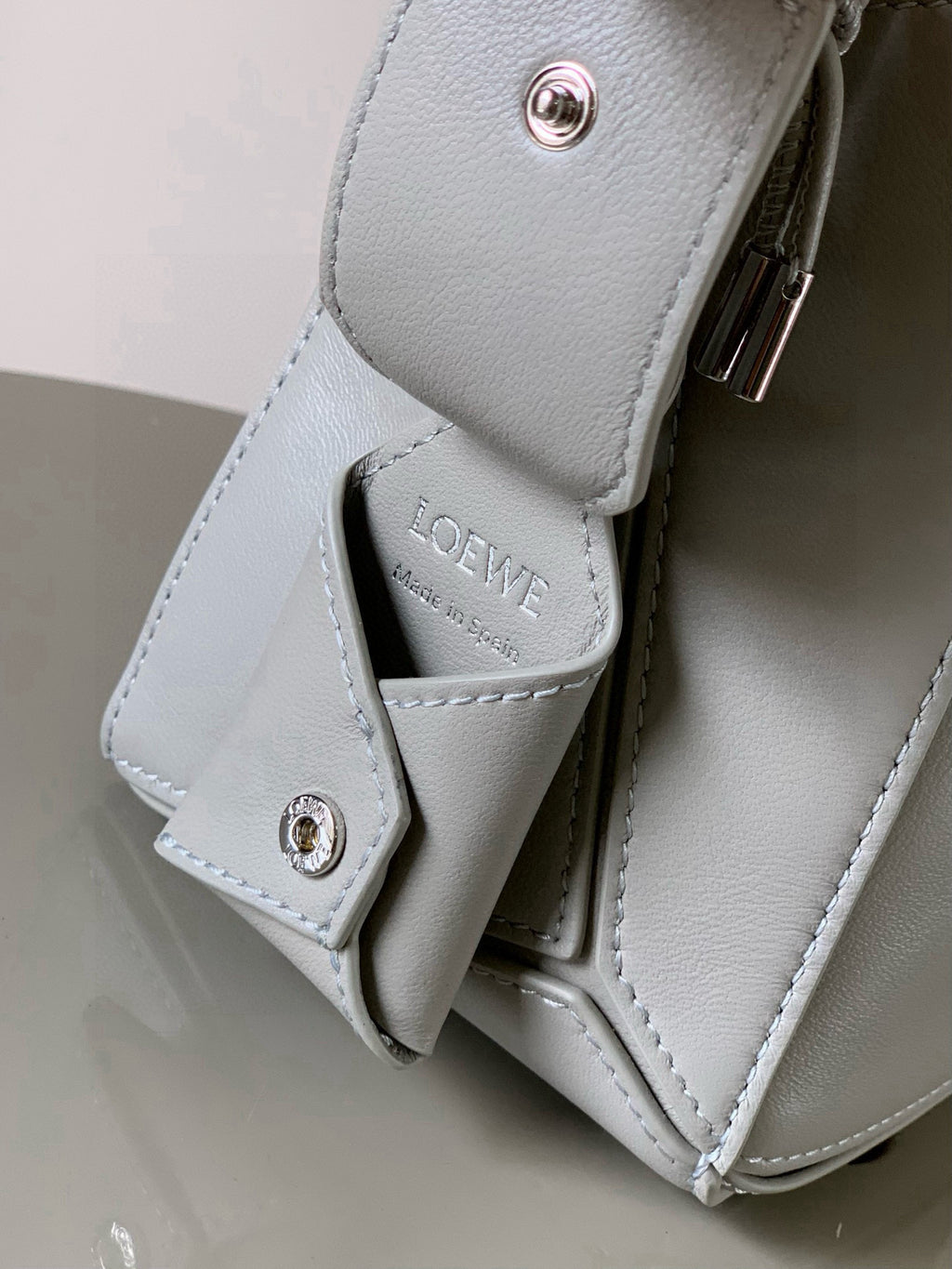 Light gray leather crossbody strap with buckles and LOEWE-printed strap tab