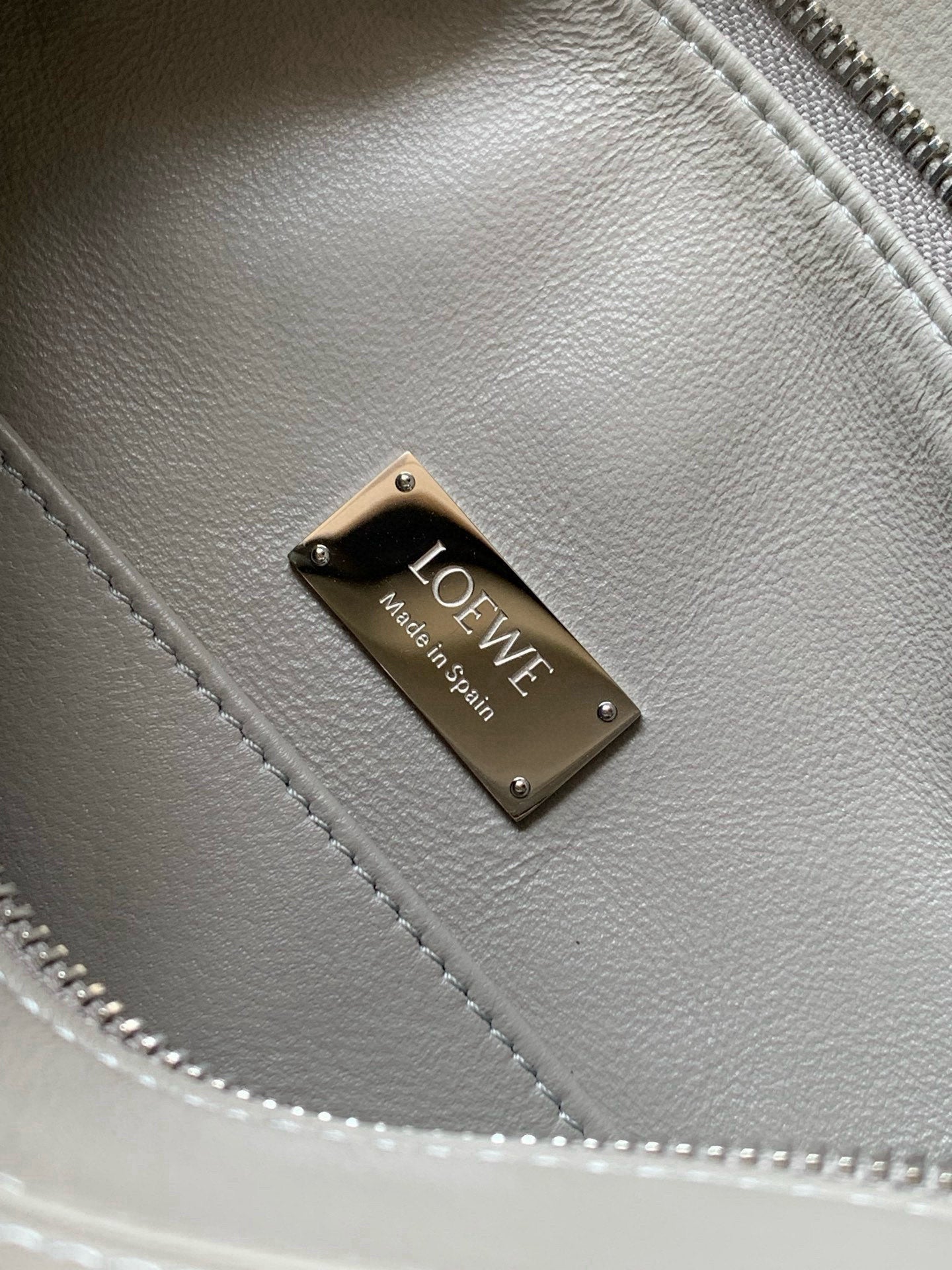 Light gray leather handbag with gold-tone LOEWE metal logo plaque on seam