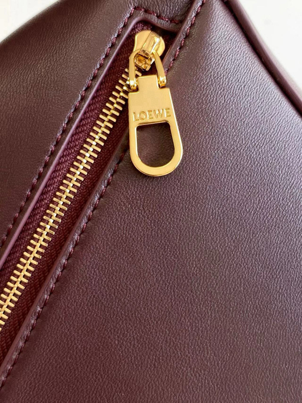 Loewe gold-tone zipper pull on dark burgundy leather bag with stitched trim