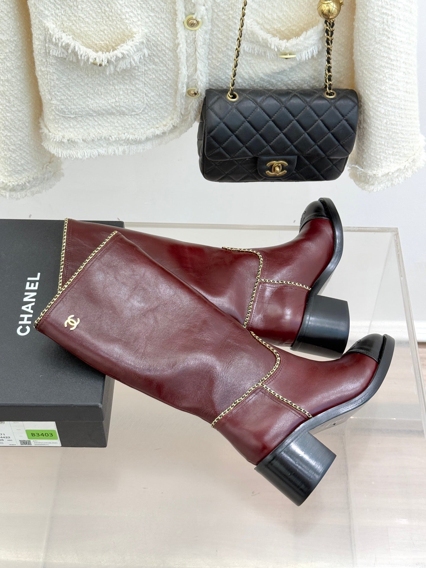 Burgundy knee-high boots laid on a box with black block heels and trim