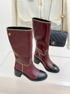 Two burgundy knee-high boots with black toe caps and gold chain trim