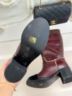 Burgundy boots with branded black soles and gold chain trim along edges