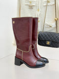 Burgundy knee-high boots with black soles and gold chain trim detail