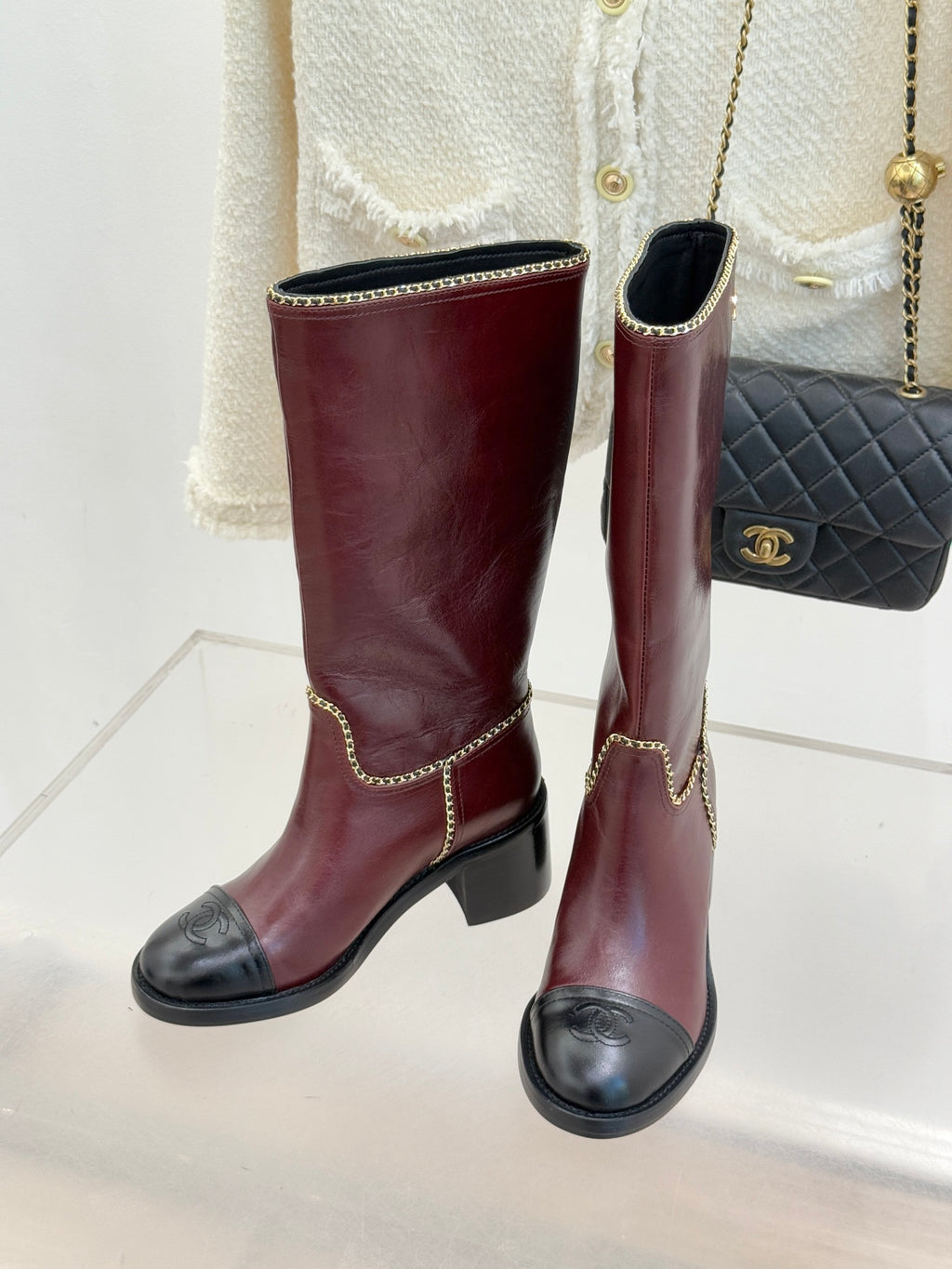 Pair of burgundy knee-high boots with black toe panels and gold chain trim