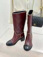 Pair of burgundy knee-high boots with black toe panels and gold chain trim