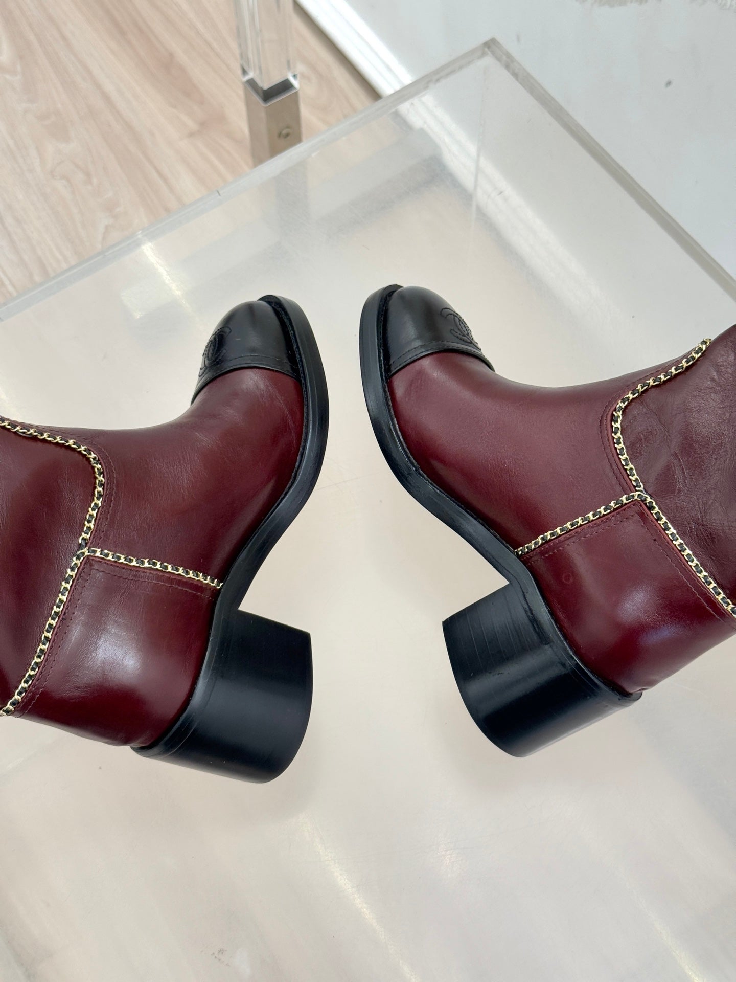 Close-up of burgundy knee-high boots with black block heels and gold chain trim