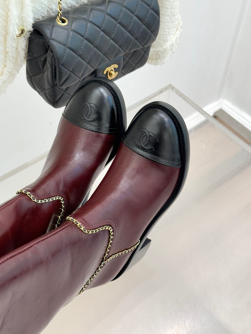 Burgundy knee-high boots with black toe panels and gold chain trim at seams