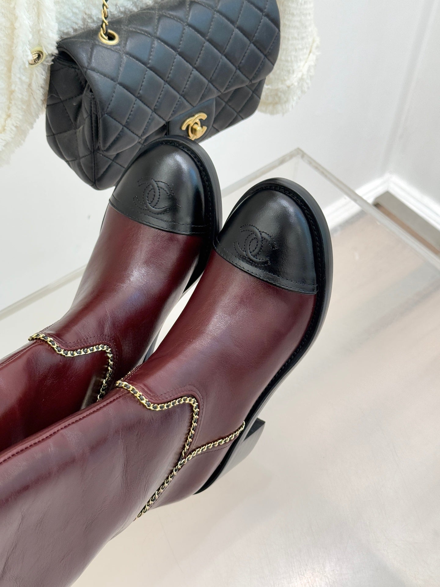 Burgundy knee-high boots with black toe panels and gold chain trim at seams