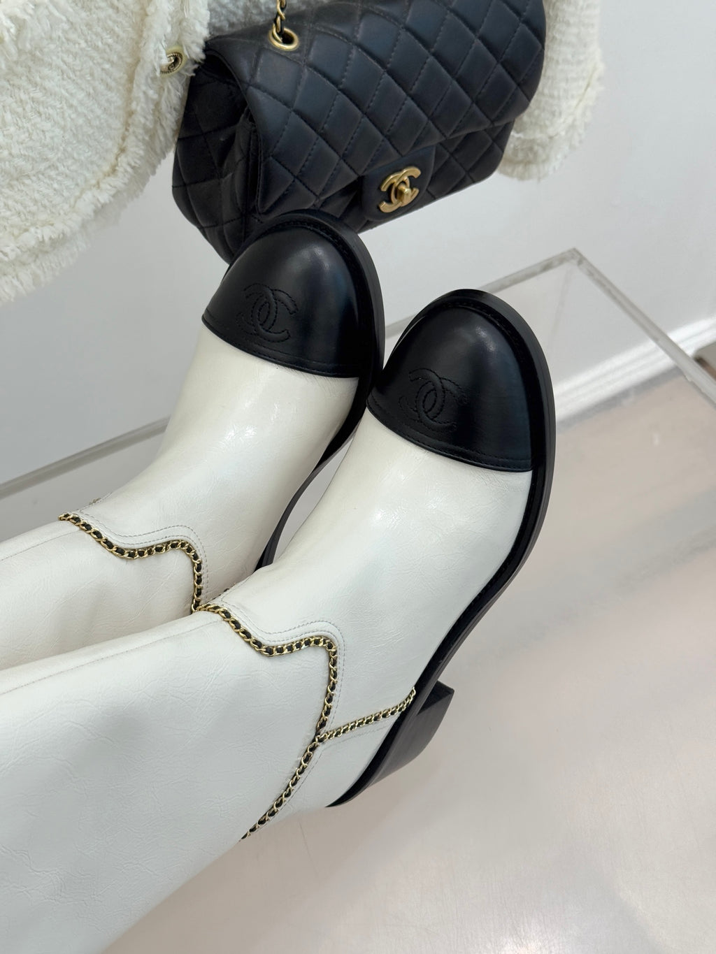 White leather knee boots with black toe panels and gold chain-trim details