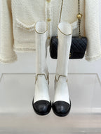 White leather knee boots with black toe panels and gold chain-trimmed cuffs