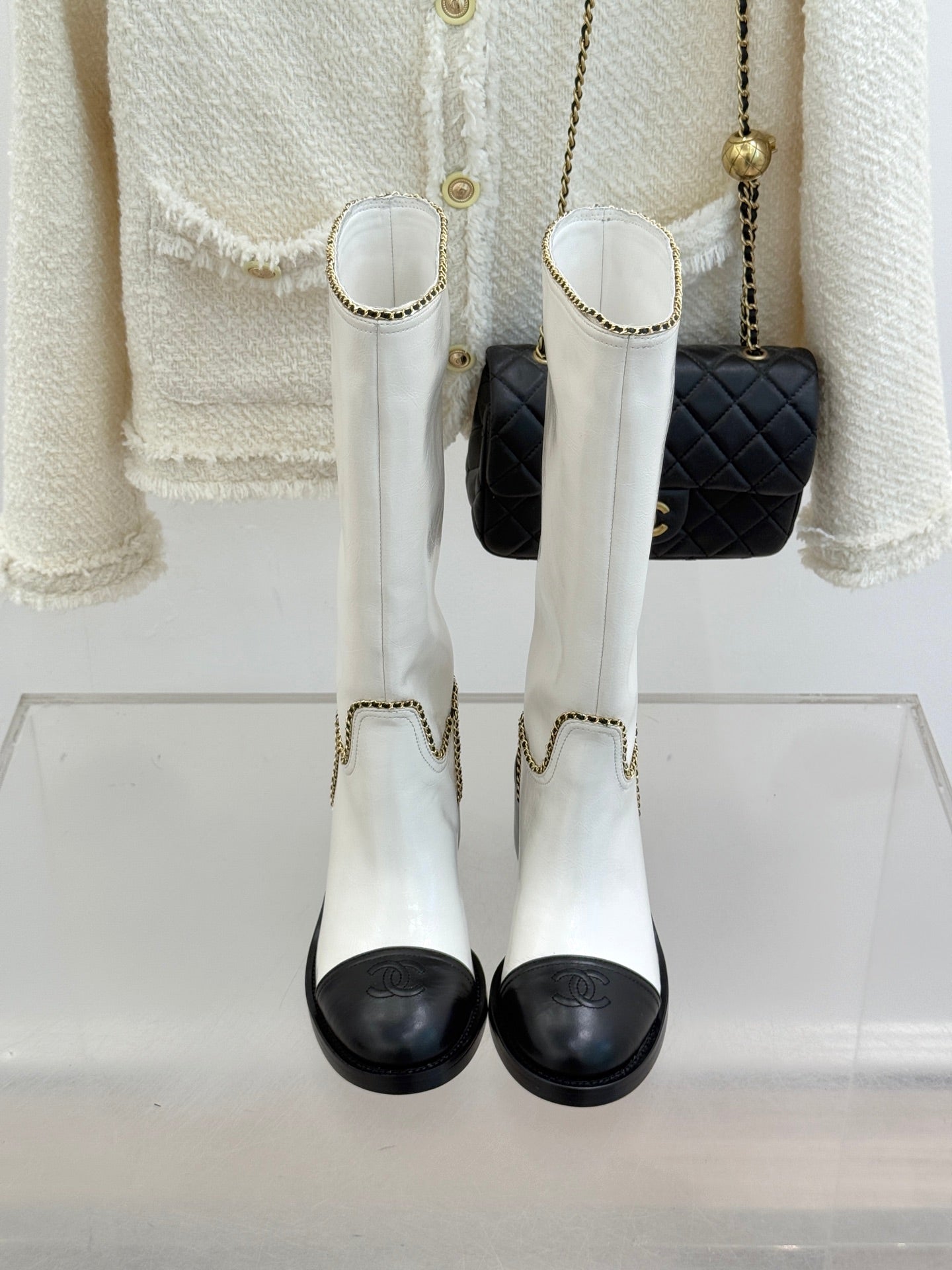 White leather knee boots with black toe panels and gold chain-trimmed cuffs