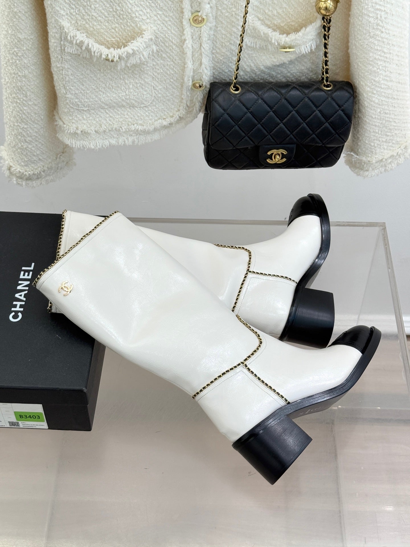 White leather knee boots with black toe panels and gold chain trim, angled side view