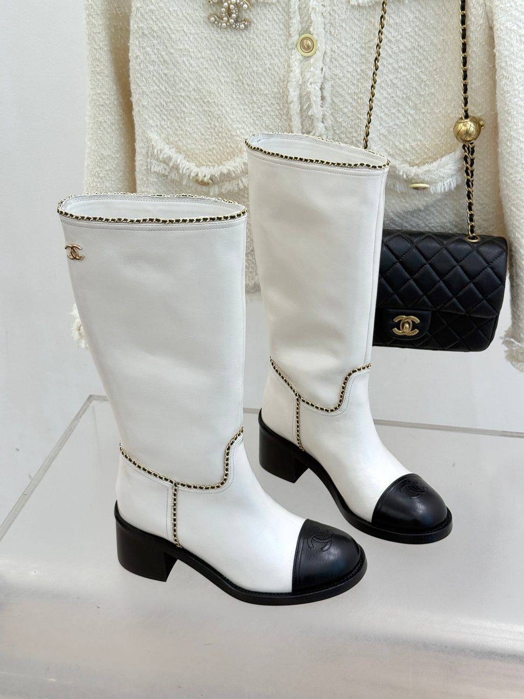 Pair of white leather knee boots with black toe panels and gold chain edge trim