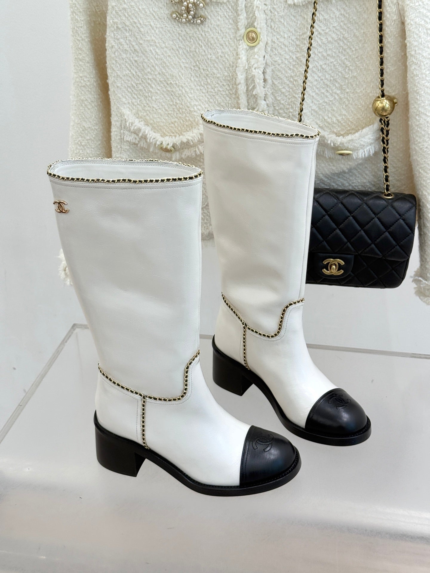 Pair of white leather knee boots with black toe panels and gold chain edge trim