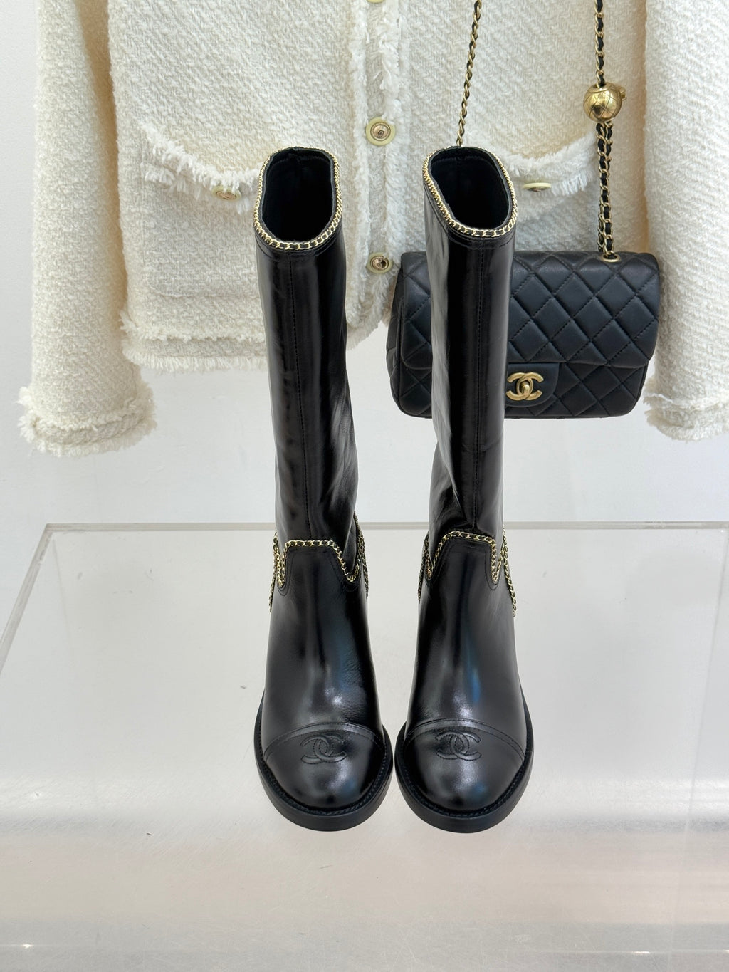 Front view of black knee-high boots with gold chain trim and round toe