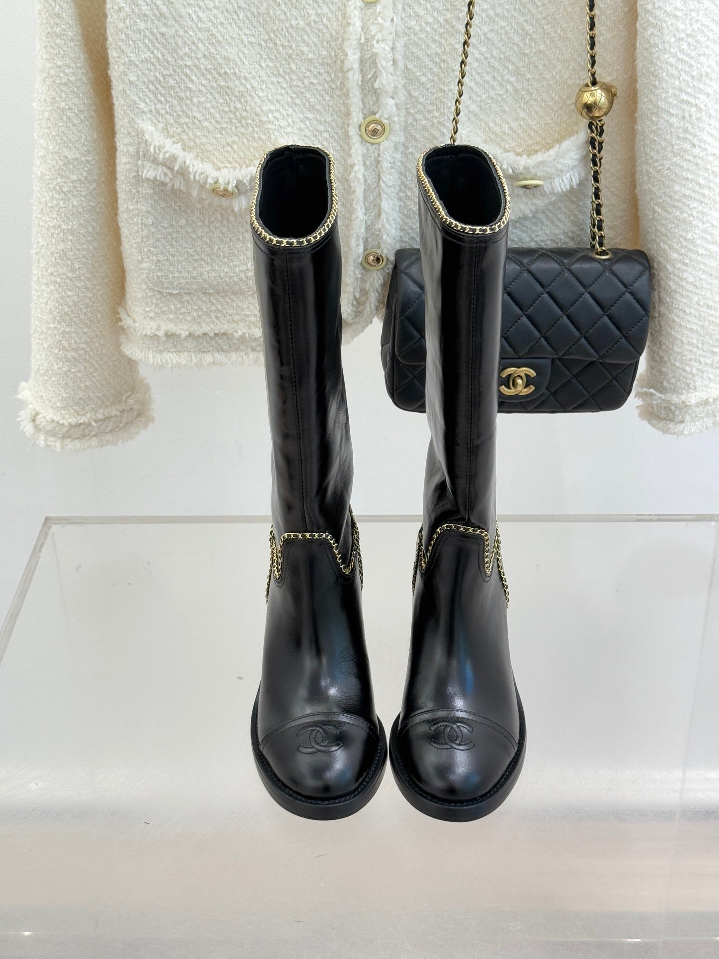 Front view of black knee-high boots with gold chain trim and round toe