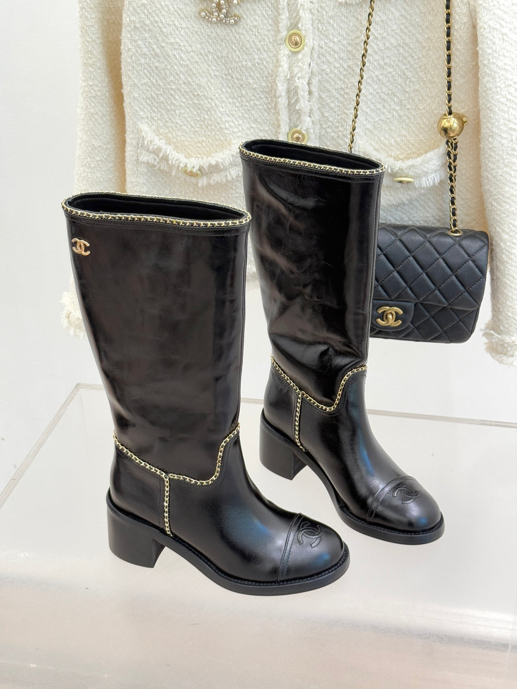 Two black knee-high boots with gold chain trim and stacked block heel