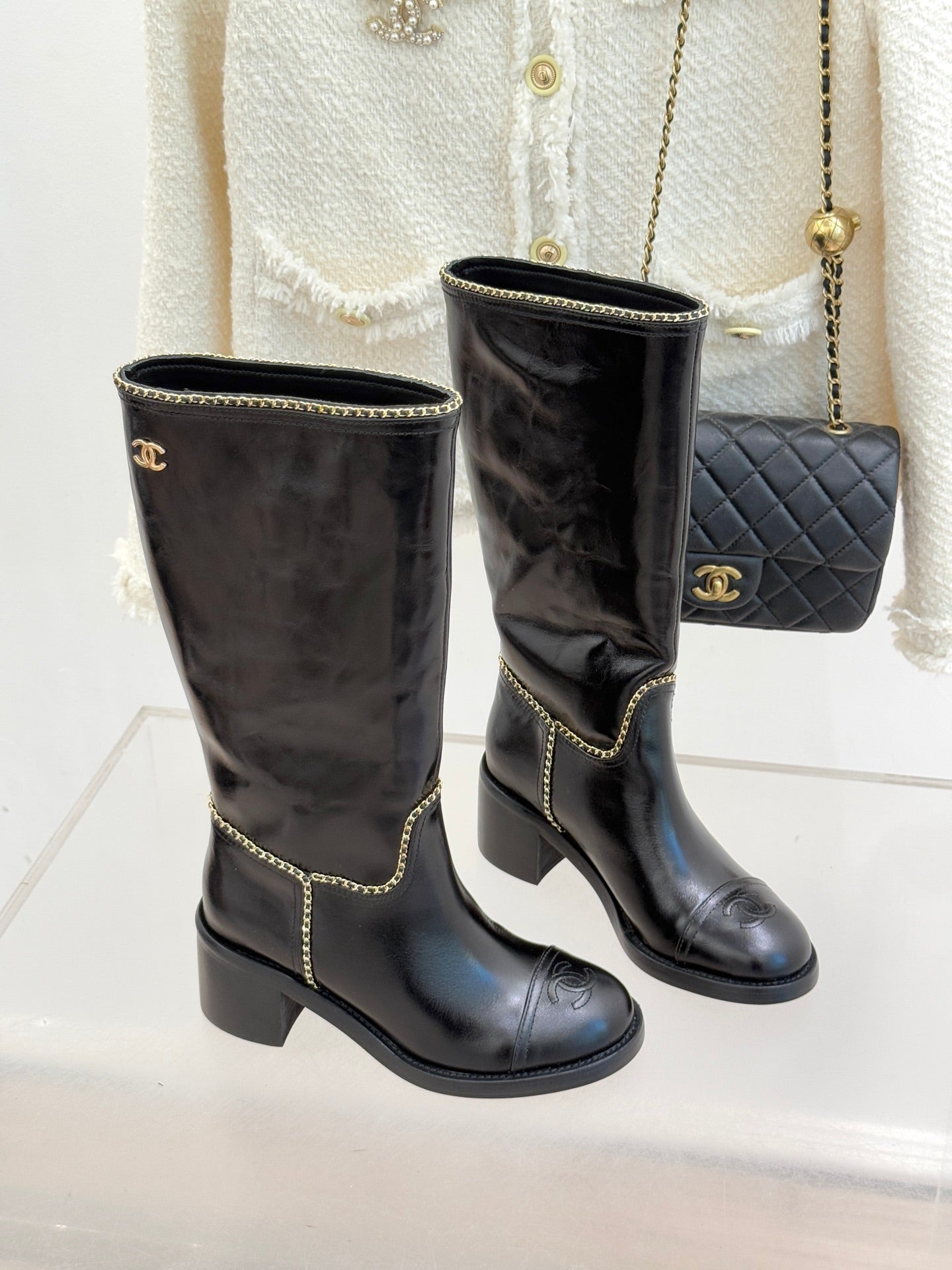Two black knee-high boots with gold chain trim and stacked block heel