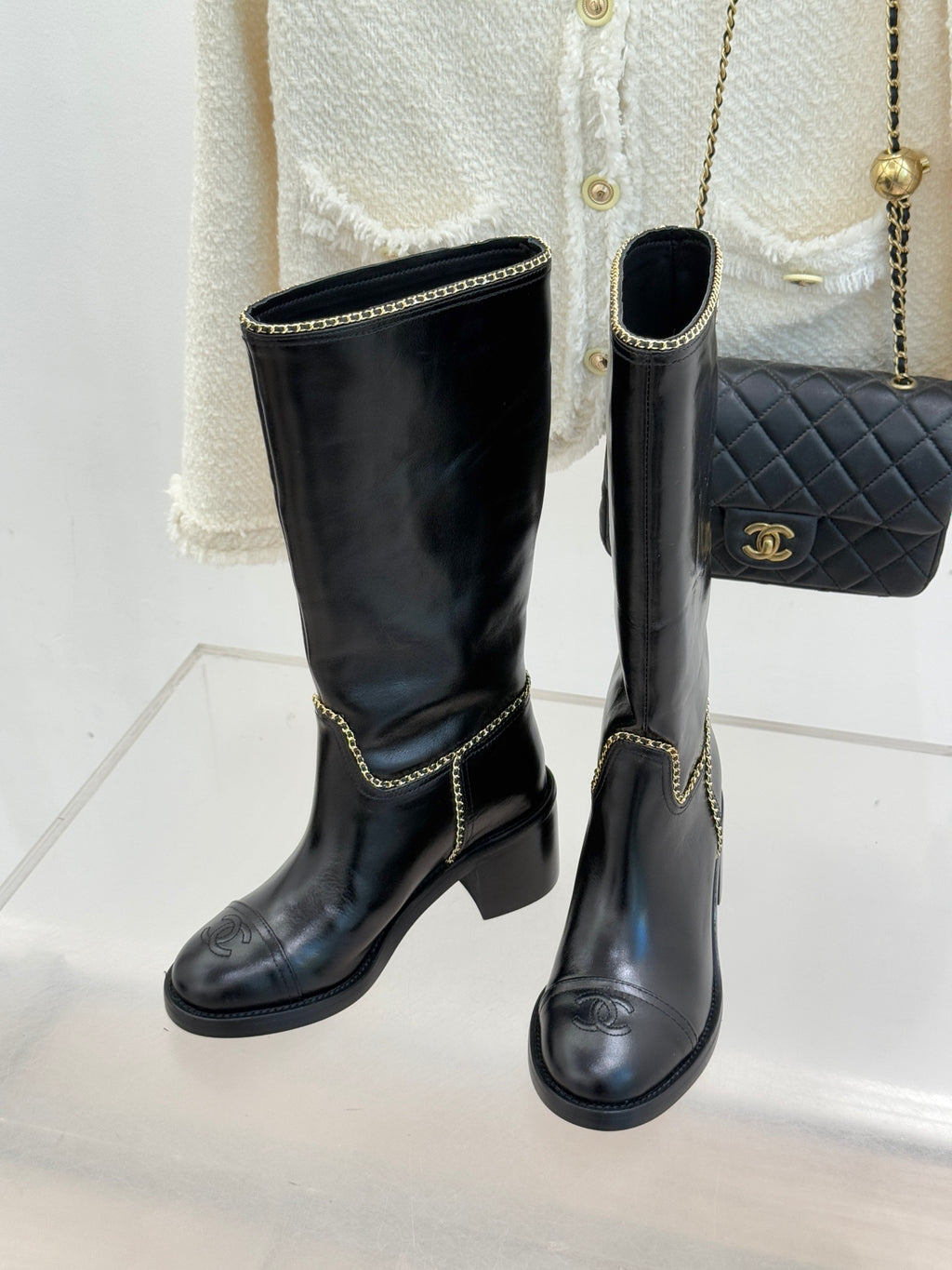 Pair of black knee-high boots with gold chain trim and low block heel