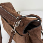 Brown suede handbag strap close-up with silver buckles and metal rings.