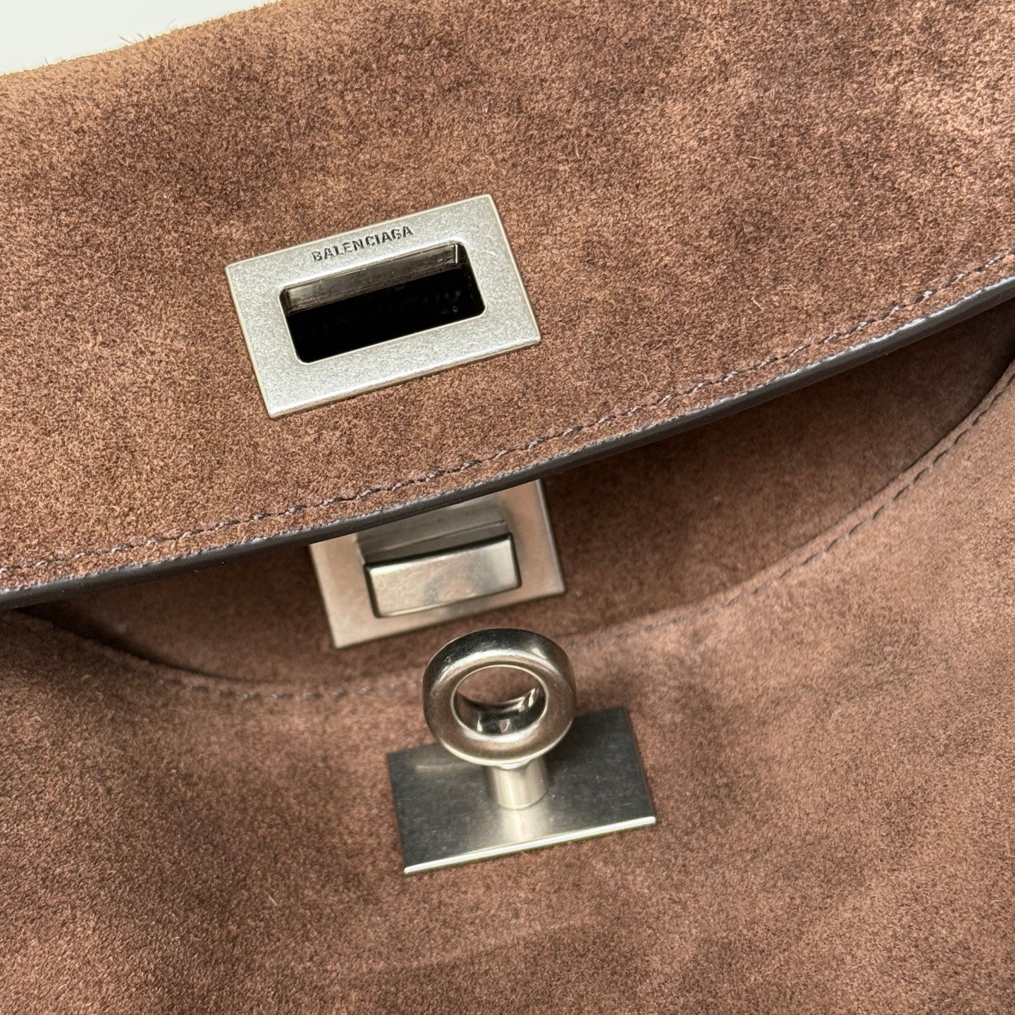 Balenciaga handbag metal logo plaque and flap hardware on brown suede.
