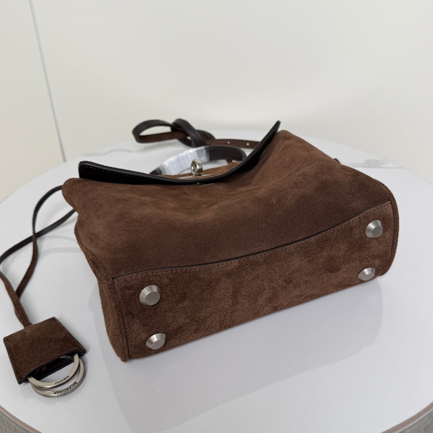 Brown suede handbag with metal studs at base and crossbody strap.