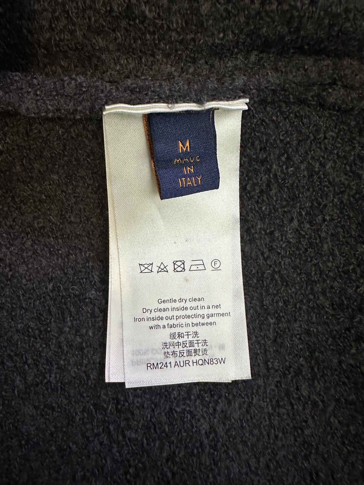 Clothing care label on dark charcoal knit sweater, size M