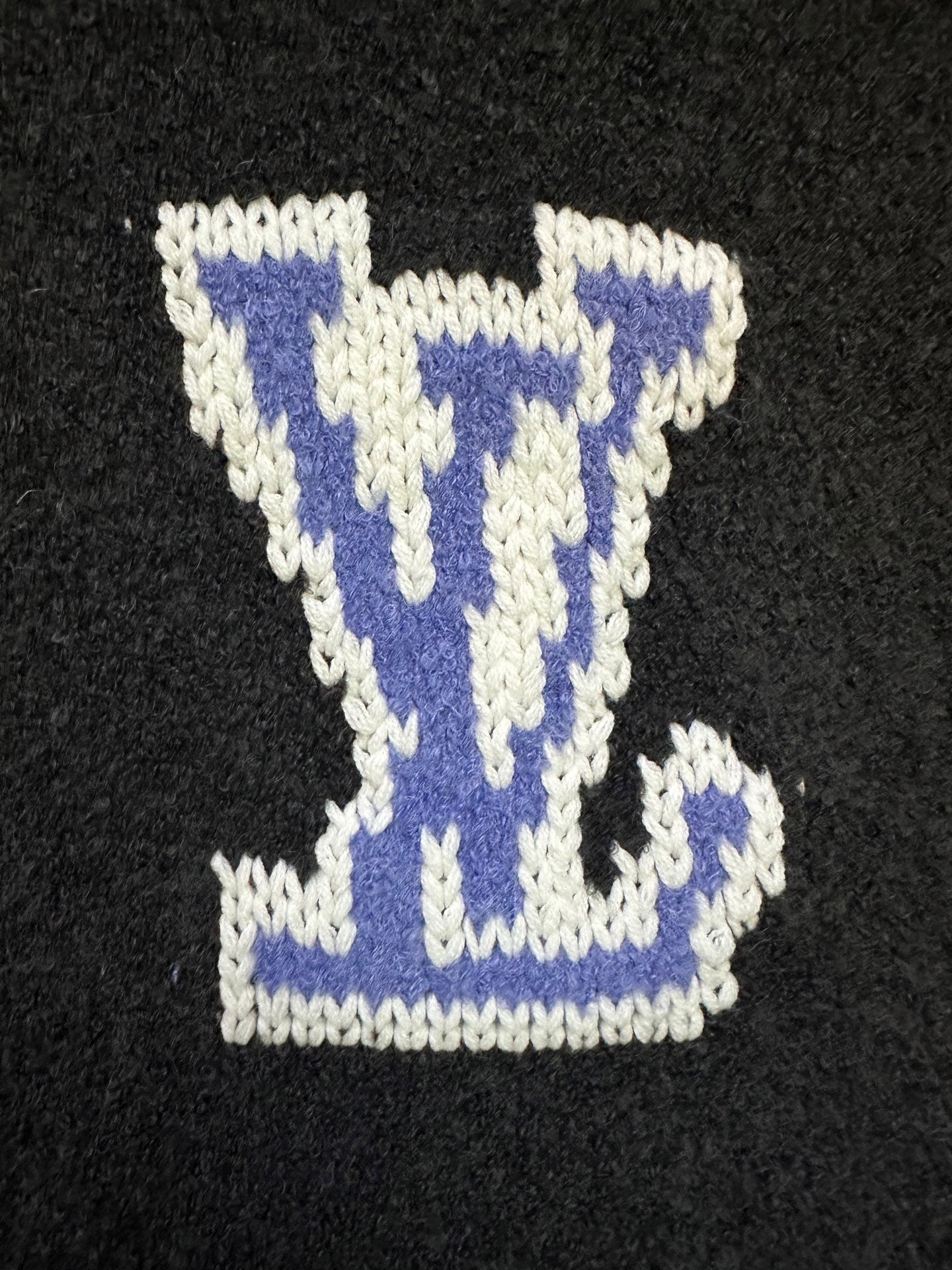 Dark charcoal knit sweater close-up of blue-and-white Louis Vuitton-style diamond logo