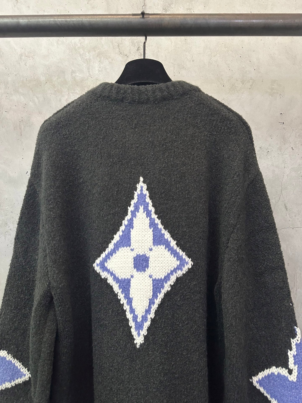 Dark charcoal knit sweater back with blue-and-white diamond monogram at upper center