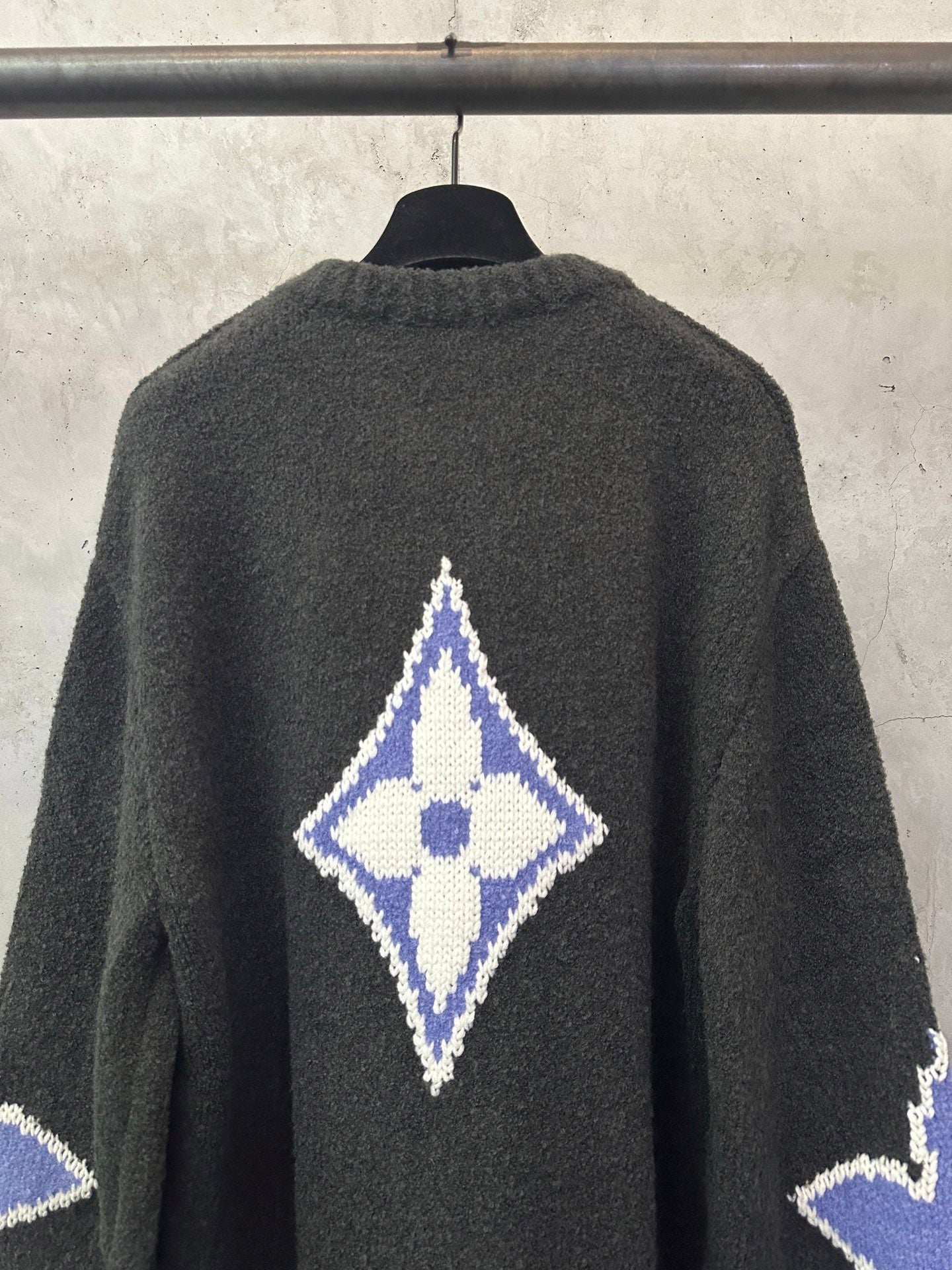Dark charcoal knit sweater back with blue-and-white diamond monogram at upper center