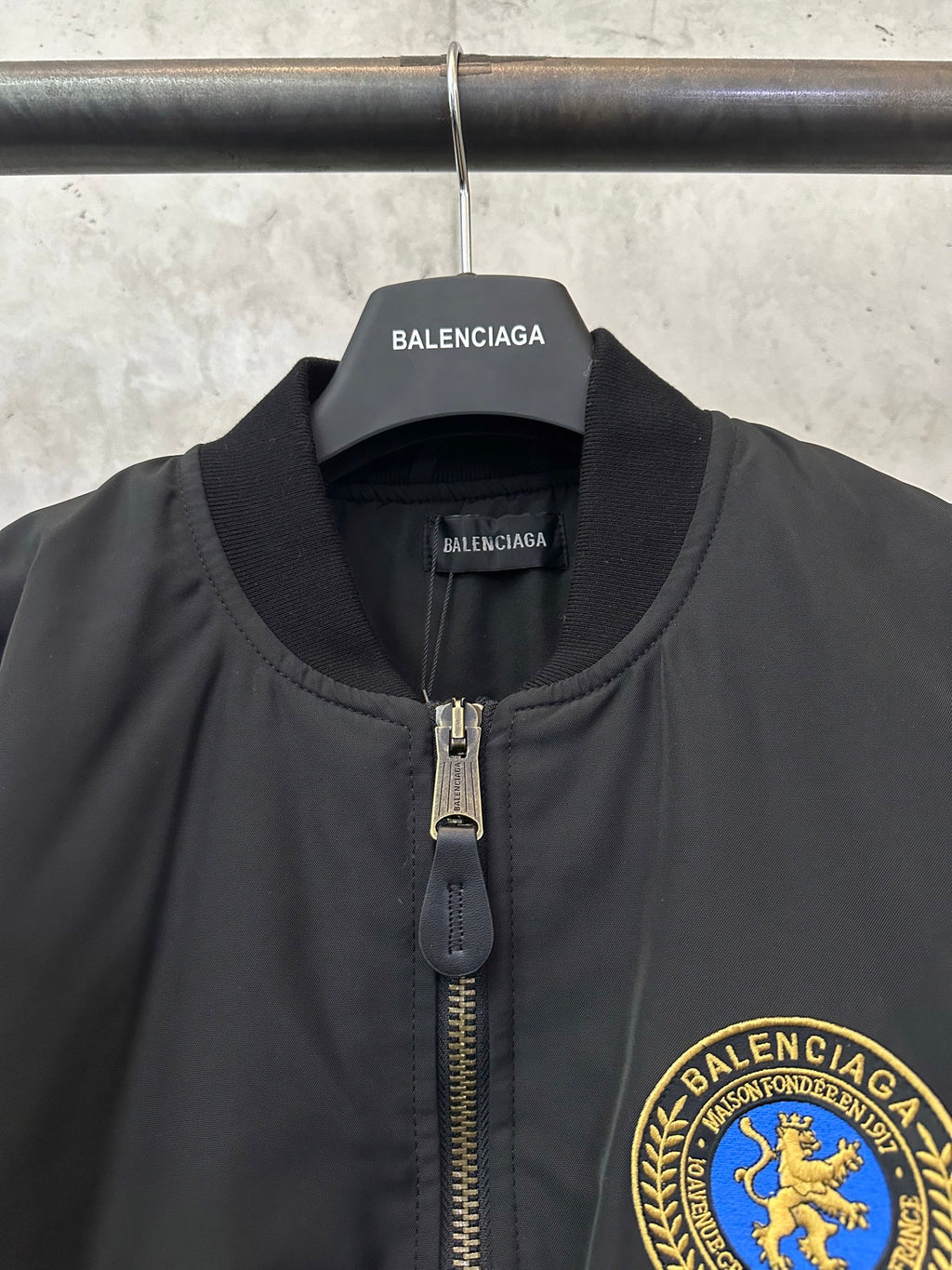 Black bomber jacket with stand collar, zip pull, and BALENCIAGA crest patch