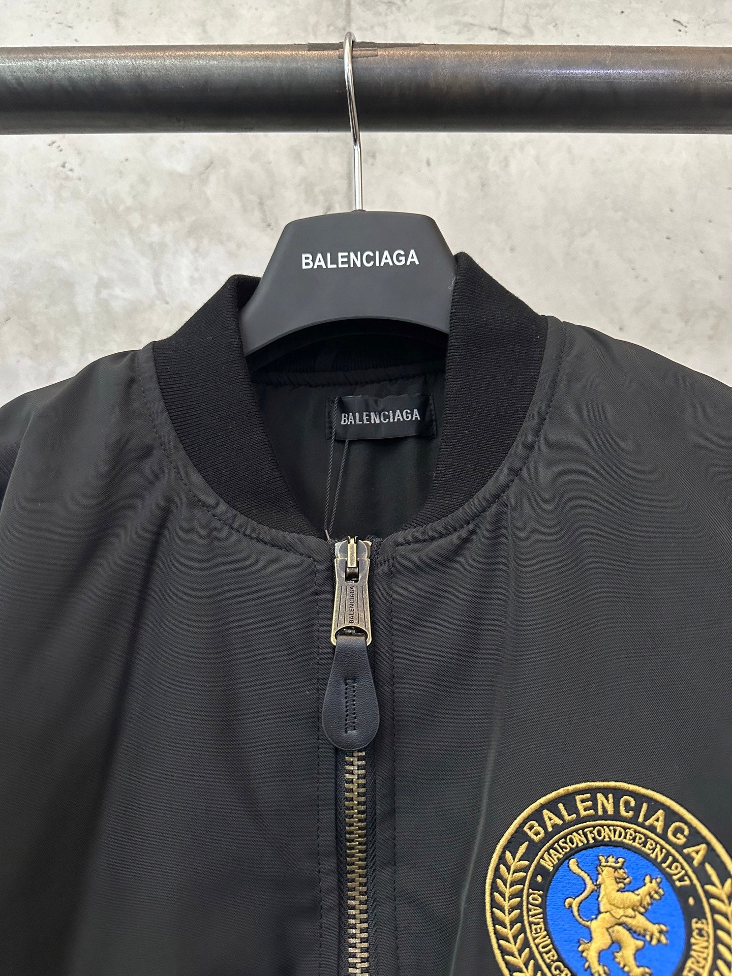 Black bomber jacket with stand collar, zip pull, and BALENCIAGA crest patch
