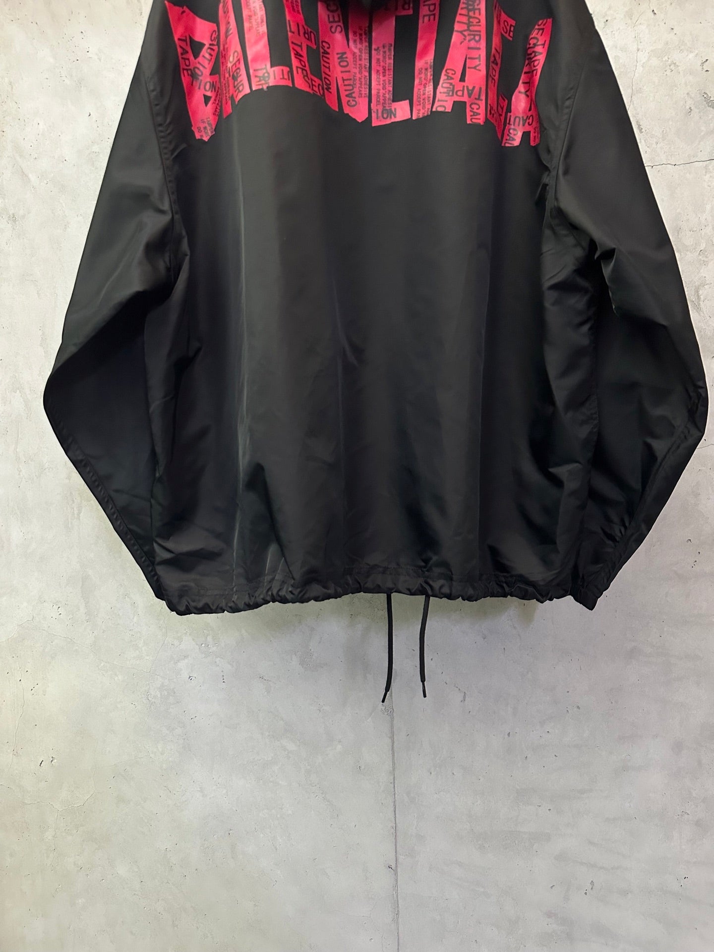 Black hooded jacket with red printed logo across upper back and drawstrings