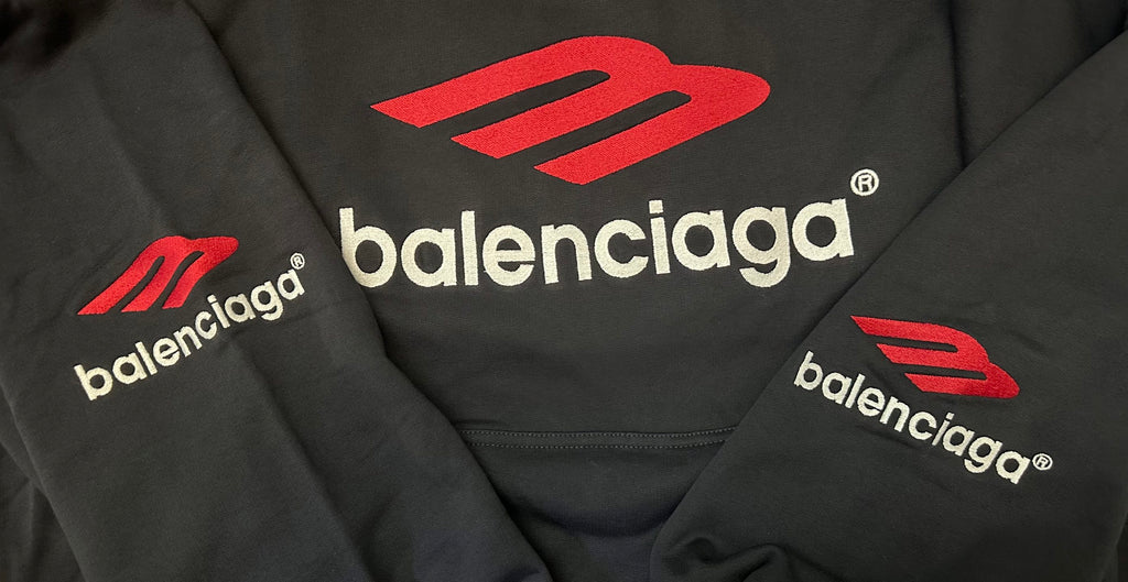 Black hoodie close-up with red Balenciaga logos and emblem branding