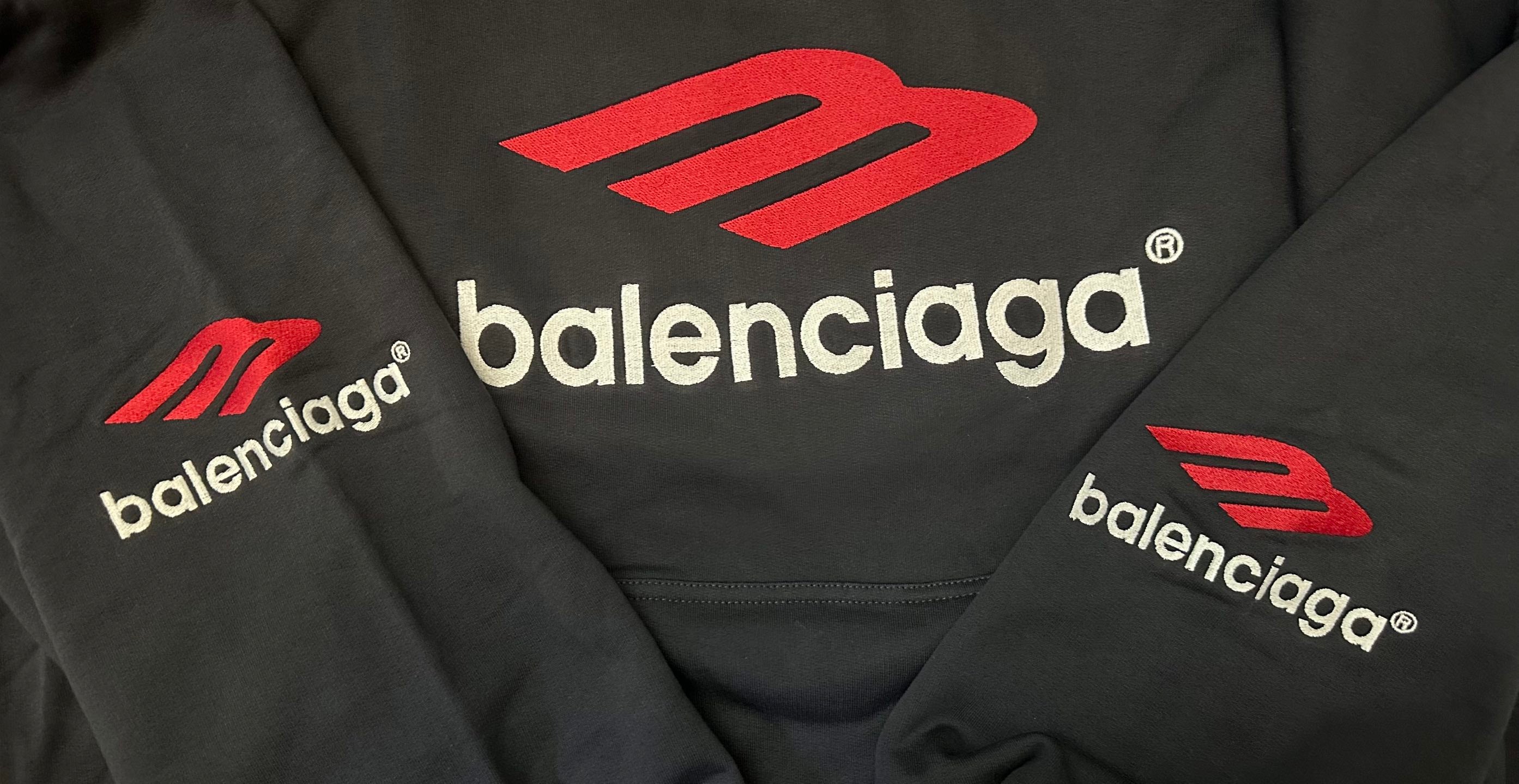 Black hoodie close-up with red Balenciaga logos and emblem branding