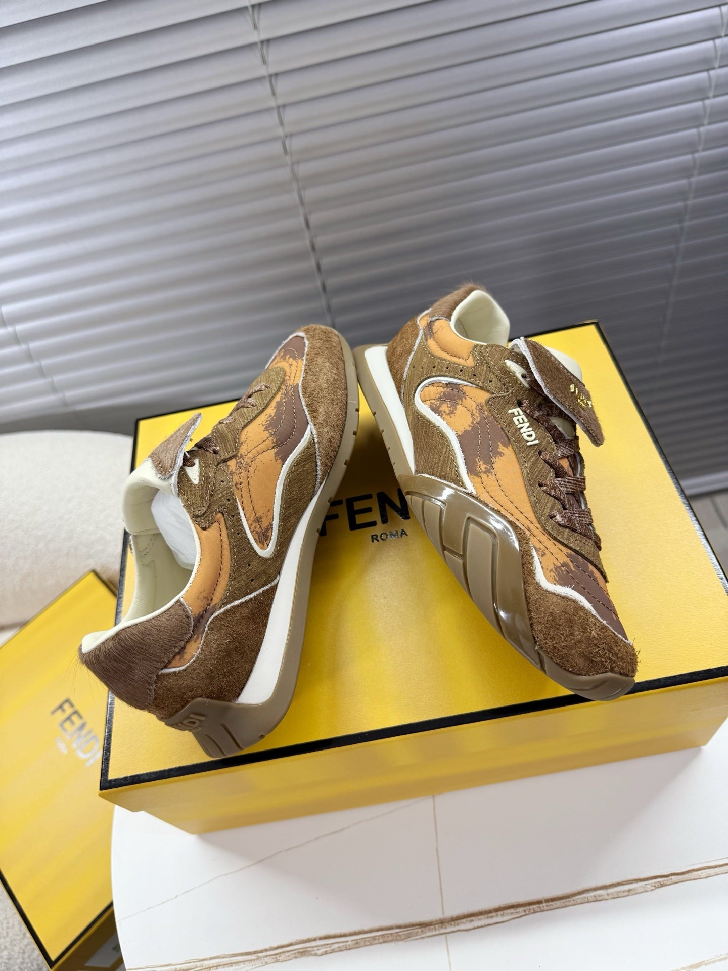 Brown lace-up low-top sneakers with white trim, angled view on yellow box